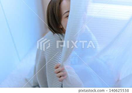 一位年輕的日本女子從窗簾後微笑。 140625538