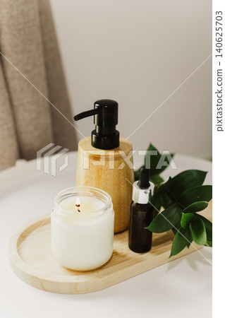 Still life of luxury spa essentials. A glass bottle with a serum, bottle with oil and candle on a table. Still life of luxury spa essentials. A glass bottle with a serum, bottle with oil and candle on a table. 140625703