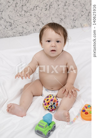 Adorable diaper baby boy sitting on white bed and reaching for toy Adorable diaper baby boy sitting on white bed and reaching for toy 140625916