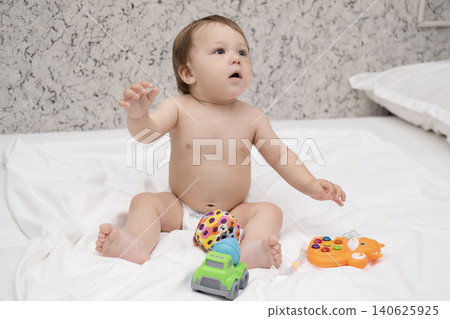Adorable diaper baby boy sitting on white bed and reaching for toy 140625925
