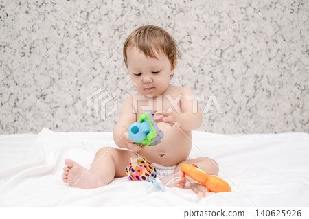 Adorable diaper baby boy sitting on white bed and reaching for toy Adorable diaper baby boy sitting on white bed and reaching for toy 140625926
