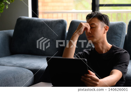 A tired man on the sofa is looking at his tablet. A tired man on the sofa is looking at his tablet. 140626001
