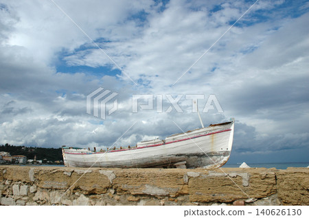 Old wooden boat pulled out of the water on a stone pier under a dramatic sky Old wooden boat pulled out of the water on a stone pier under a dramatic sky 140626130