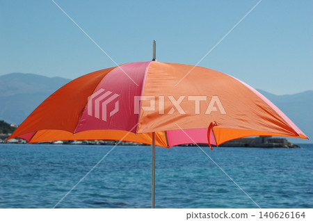 Bright orange and pink beach umbrella against blue sea water Bright orange and pink beach umbrella against blue sea water 140626164