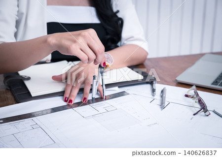 Female architect using dividers working on blueprint architects project in office. Female architect using dividers working on blueprint architects project in office. 140626837