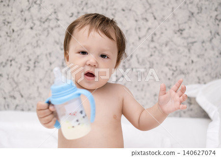 Cute shirtless baby boy holding a baby bottle with milk or formula on bed Cute shirtless baby boy holding a baby bottle with milk or formula on bed 140627074