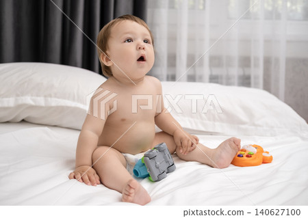 Adorable diaper baby boy sitting on white bed and reaching for toy Adorable diaper baby boy sitting on white bed and reaching for toy 140627100