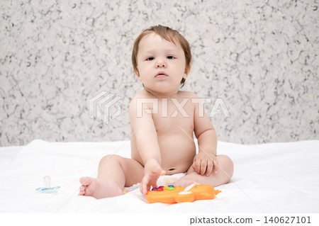 Adorable diaper baby boy sitting on white bed and reaching for toy Adorable diaper baby boy sitting on white bed and reaching for toy 140627101