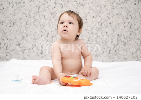 Adorable diaper baby boy sitting on white bed and reaching for toy Adorable diaper baby boy sitting on white bed and reaching for toy 140627102