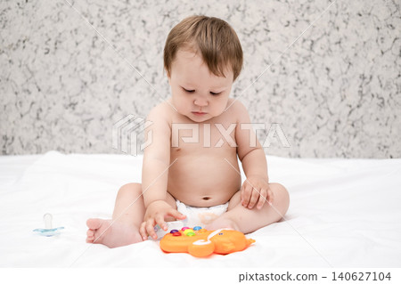 Adorable diaper baby boy sitting on white bed and reaching for toy Adorable diaper baby boy sitting on white bed and reaching for toy 140627104