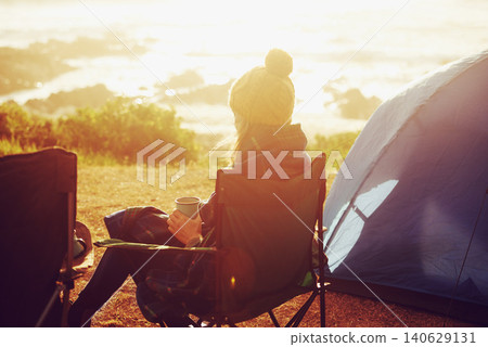 Sunset, camping and woman by tent on vacation, adventure or holiday in nature for travel. Evening, coffee and back of female person relaxing and drinking cappuccino in chair outdoor for weekend trip. Sunset, camping and woman by tent on vacation, adventure or holiday in nature for travel. Evening, coffee and back of female person relaxing and drinking cappuccino in chair outdoor for weekend trip. 140629131