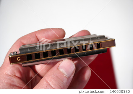 Hand holding a silver and brown ten hole harmonica in C major Hand holding a silver and brown ten hole harmonica in C major 140630580