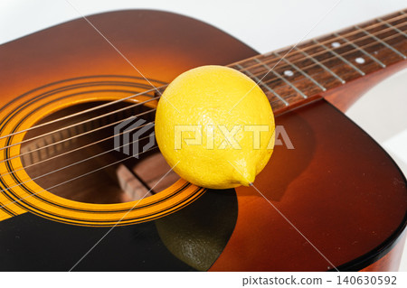 Whole yellow lemon resting on the strings of an acoustic guitar Whole yellow lemon resting on the strings of an acoustic guitar 140630592