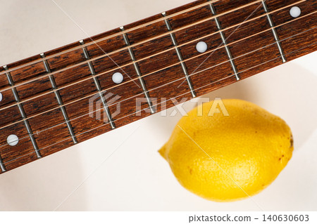 Acoustic guitar fretboard with steel strings and a whole yellow lemon Acoustic guitar fretboard with steel strings and a whole yellow lemon 140630603