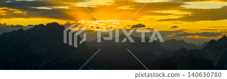 Brilliant sun rays stream through clouds above the Dolomite mountains at sunset. Glowing alpine landscape with layered peaks, atmospheric haze and spectacular natural light. Brilliant sun rays stream through clouds above the Dolomite mountains at sunset. Glowing alpine landscape with layered peaks, atmospheric haze and spectacular natural light. 140630780
