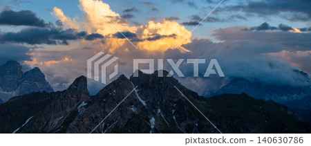 Dramatic storm clouds engulf rugged Dolomite mountain peaks at sunset in northern Italy. Moody alpine landscape with glowing sky, rocky ridges and breathtaking natural scenery. Dramatic storm clouds engulf rugged Dolomite mountain peaks at sunset in northern Italy. Moody alpine landscape with glowing sky, rocky ridges and breathtaking natural scenery. 140630786