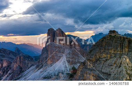 Dramatic storm clouds gather above Cinque Torri and Rifugio Nuvolau in the Italian Dolomites. Panoramic mountain landscape with rugged limestone peaks and glowing sunset light. Dramatic storm clouds gather above Cinque Torri and Rifugio Nuvolau in the Italian Dolomites. Panoramic mountain landscape with rugged limestone peaks and glowing sunset light. 140630788