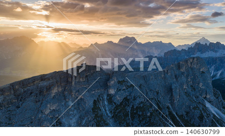 Golden sun rays illuminate the Dolomite mountains near Rifugio Nuvolau at sunset. Atmospheric alpine landscape with rugged limestone cliffs, distant peaks and dramatic light. 140630799