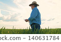 Modern agriculture worker, Farmer inspecting cereal plants, Wheat farming in summer, Outdoor work in agriculture, Farming and food production, Agricultural professional at field, Farming clothes and 140631784