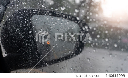 Close-up view looking through a dark car side mirror covered in heavy raindrops during a storm. Water splashes blur the bright window backdrop view entirely. Close-up view looking through a dark car side mirror covered in heavy raindrops during a storm. Water splashes blur the bright window backdrop view entirely. 140633999