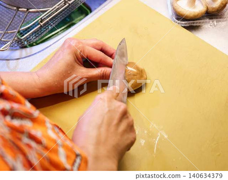 A woman cutting shiitake mushrooms with a kitchen knife. 140634379