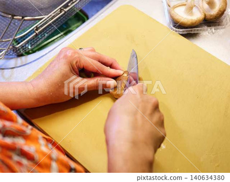 A woman cutting shiitake mushrooms with a kitchen knife. 140634380