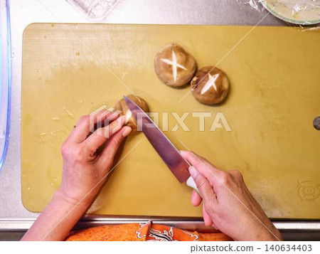 A woman cutting shiitake mushrooms with a kitchen knife. 140634403