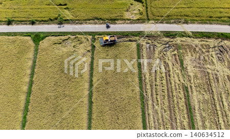 High angle view of a combine harvester while harvesting rice crops in rice field. Combine harvesters are agricultural machines mainly used to harvest grain crops such as cereals. High angle view of a combine harvester while harvesting rice crops in rice field. Combine harvesters are agricultural machines mainly used to harvest grain crops such as cereals. 140634512