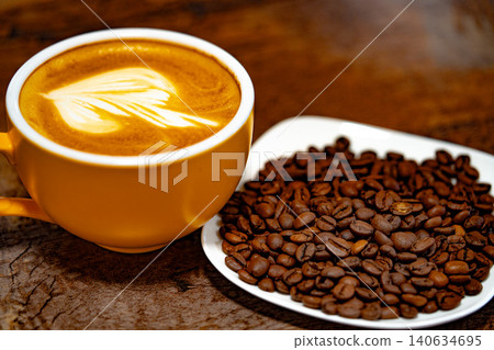 Cup of coffee decorated with a heart and coffee beans on a white plate. dark background Cup of coffee decorated with a heart and coffee beans on a white plate. dark background 140634695