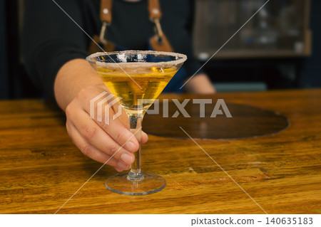 A bartender offers a freshly prepared Martini on the wooden bar of a pub, evoking summer nights with friends A bartender offers a freshly prepared Martini on the wooden bar of a pub, evoking summer nights with friends 140635183