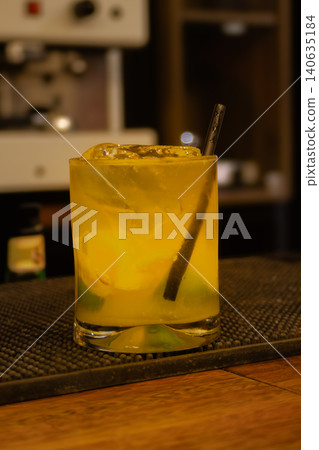 Yellow cocktail with ice and a straw on a wooden bar counter, chilled and ready for an evening aperitif or celebration 140635184