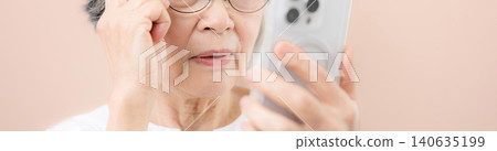 一位頭髮花白的老婦人戴著老花眼鏡,正對著粉紅色背景上的智慧型手機螢幕;螢幕上的文字難以辨認,她看起來很苦惱,懷疑自己是不是遇到了騙局。 一位頭髮花白的老婦人戴著老花眼鏡,正對著粉紅色背景上的智慧型手機螢幕;螢幕上的文字難以辨認,她看起來很苦惱,懷疑自己是不是遇到了騙局。 140635199