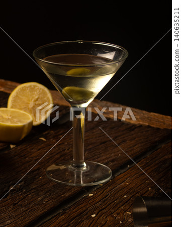 Martini cocktail with olive and lemon slice on dark rustic wooden table ,elegant gourmet still life for evening bar setting Martini cocktail with olive and lemon slice on dark rustic wooden table ,elegant gourmet still life for evening bar setting 140635211