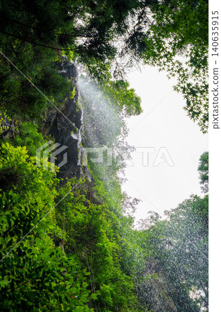 The flowing water of a waterfall surrounded by fresh greenery The flowing water of a waterfall surrounded by fresh greenery 140635915
