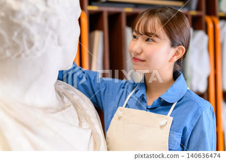 A woman in an apron gazes at a plaster cast. 140636474