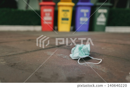 Used medical face mask discard on pavement floor on blurred recycle bin or trash. Medical waste disposal with unhygienic. Disposable earloop face mask waste garbage on floor. Green surgical face mask. Used medical face mask discard on pavement floor on blurred recycle bin or trash. Medical waste disposal with unhygienic. Disposable earloop face mask waste garbage on floor. Green surgical face mask. 140640220