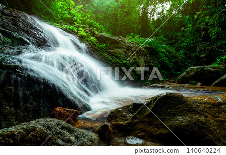 Beautiful waterfall in jungle. Waterfall in tropical forest with green tree and sunlight. Waterfall is flowing in jungle. Nature background. Rock or stone at waterfall. Long exposure photography. 140640224
