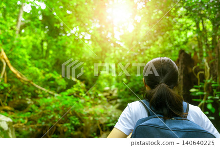 Happy asian woman with backpack travel in green forest. Adventure travel. Minimal life. Back view of black long hair woman with white shirt in tropical forest for vacation. Active girl in the woods. 140640225