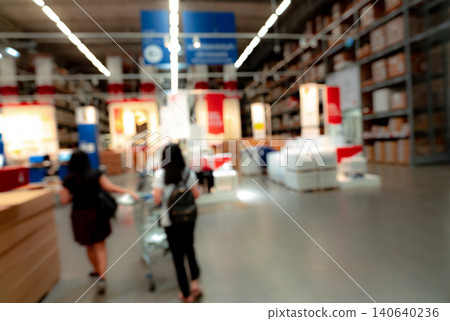 Blurred two woman shopping goods at self-service warehouse of store. Woman pushing a shopping cart in warehouse. Blur rows of shelves with storage box on rack in warehouse. Stock of products. Blurred two woman shopping goods at self-service warehouse of store. Woman pushing a shopping cart in warehouse. Blur rows of shelves with storage box on rack in warehouse. Stock of products. 140640236