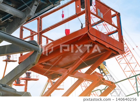 Articulated orange boom lift. Aerial platform lift. Telescopic boom lift against the blue sky. Maintenance and repair hydraulic boom lift service concept. Crane dealership background. Articulated orange boom lift. Aerial platform lift. Telescopic boom lift against the blue sky. Maintenance and repair hydraulic boom lift service concept. Crane dealership background. 140640256