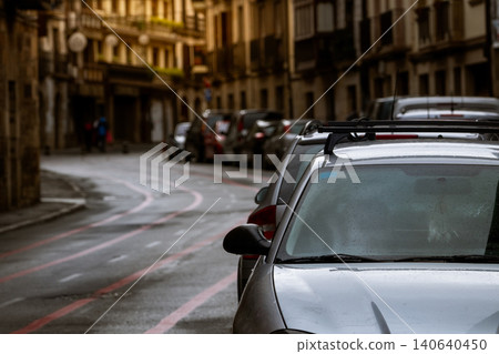 Row of cars parked along the street and old buildings in Europe city. Many cars parked on road in old town. City street in Europe. Front view of car parked outside residential building. City traffic. Row of cars parked along the street and old buildings in Europe city. Many cars parked on road in old town. City street in Europe. Front view of car parked outside residential building. City traffic. 140640450