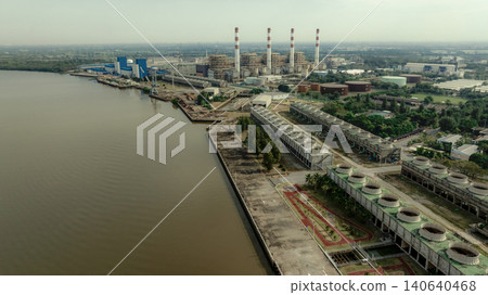 Aerial drone view of large industrial power plant and energy facility beside river waterfront, electricity generation infrastructure with smokestacks cooling systems and heavy industrial production. Aerial drone view of large industrial power plant and energy facility beside river waterfront, electricity generation infrastructure with smokestacks cooling systems and heavy industrial production. 140640468