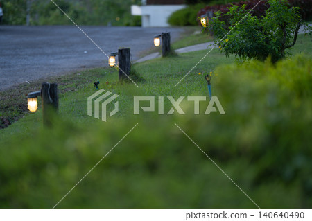 Garden pathway lighting along a landscaped lawn at dusk, decorative outdoor lamps. Illumination for residential property, hospitality design. Sustainable living. Resort environment and relaxing. 140640490