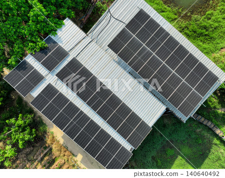 Aerial drone view of solar panel installation on metal rooftop of rural house and green landscape. Renewable energy system generating electricity for sustainable living and reducing carbon emission. 140640492