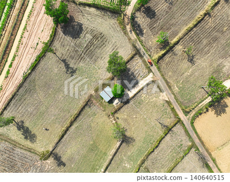 Drone view of rural farmland with geometric field patterns, dry soil and irrigation canal, small hut and dirt road intersection, agriculture landscape showing cultivation and countryside environment. Drone view of rural farmland with geometric field patterns, dry soil and irrigation canal, small hut and dirt road intersection, agriculture landscape showing cultivation and countryside environment. 140640515