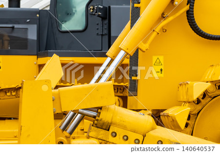 Close up hydraulic system of yellow bulldozer at industrial construction site, heavy machinery engineering detail with mechanical cylinder and steel component for infrastructure and excavation work. Close up hydraulic system of yellow bulldozer at industrial construction site, heavy machinery engineering detail with mechanical cylinder and steel component for infrastructure and excavation work. 140640537