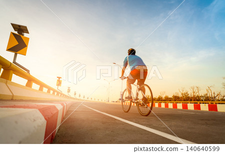 Blur back view of a man wear helmet ride a bicycle for exercise. Curve road traffic sign with people cycling bike on the road. Outdoor activity in summer. Healthy lifestyle. Sport and activity. Blur back view of a man wear helmet ride a bicycle for exercise. Curve road traffic sign with people cycling bike on the road. Outdoor activity in summer. Healthy lifestyle. Sport and activity. 140640599