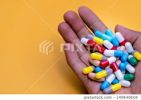 Man hand holding colorful capsule pills on yellow background. Prescription drugs. Drug overuse and polypharmacy concept. Drug allergy. Pharmaceutical industry. Pharmacy banner. Healthcare and medicine Man hand holding colorful capsule pills on yellow background. Prescription drugs. Drug overuse and polypharmacy concept. Drug allergy. Pharmaceutical industry. Pharmacy banner. Healthcare and medicine 140640608