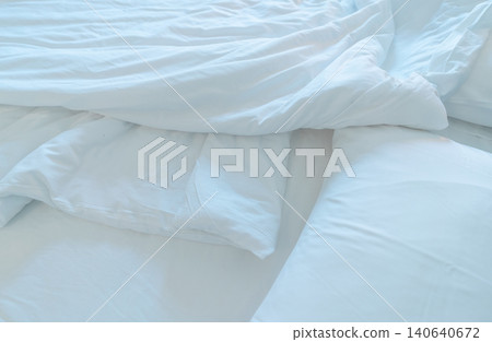 White comfort bed and soft pillow in modern bedroom. White linen blanket in hotel bedroom. Closeup detail of messy white blanket after waking up in morning. Comfortable bed with soft white duvet. 140640672
