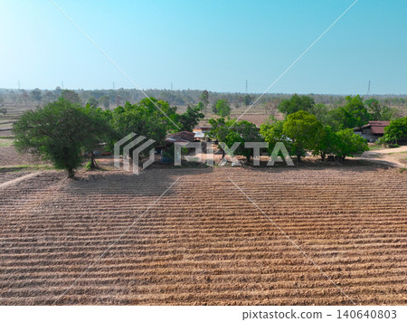 Aerial view of rural farmland with cultivated agricultural field and village homestead surrounded by green trees, drone landscape showcasing sustainable farming environment. Sustainable land use. Aerial view of rural farmland with cultivated agricultural field and village homestead surrounded by green trees, drone landscape showcasing sustainable farming environment. Sustainable land use. 140640803